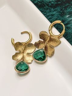 Elevate your style with these exquisite gold floral earrings. Featuring a delicate flower motif, these earrings are adorned with a stunning emerald green gemstone that adds a touch of elegance and sophistication. The intricate detailing on the gold petals complements the vibrant hue of the gemstone, making these earrings a perfect accessory for any occasion. Crafted with precision and care, these earrings are sure to become a cherished addition to your jewelry collection. Whether you're dressing Flower Motif, Green Flower, Green Gemstones, Gold Floral, Delicate Flower, Floral Earrings, Green Flowers, Timeless Beauty, Emerald Green