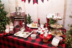 a red and black table topped with food next to a christmas tree filled with presents