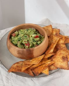 a bowl of guacamole and tortilla chips on a silver plate