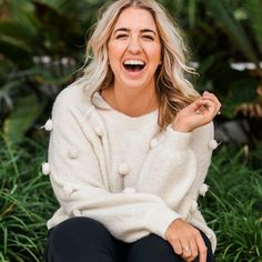 a woman sitting on the ground laughing and holding her hand up to her mouth with both hands