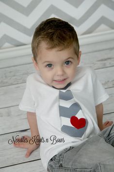 a little boy sitting on the floor wearing a tie with a heart painted on it