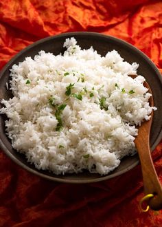 rice in a bowl with a wooden spoon on an orange tablecloth, ready to be eaten