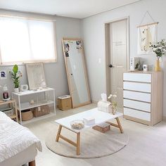 a bedroom with white walls and furniture in the room, including a bed, dresser, mirror, chest of drawers, and coffee table