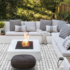 a white couch sitting on top of a patio next to a fire pit with pillows