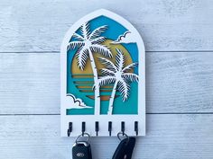 a pair of scissors hanging from a wall with palm trees and the sun in the background