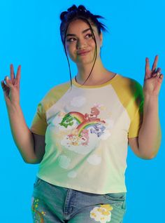 Channel some Funshine Bear vibes to your wardrobe! This sunny baby tee features a vintage print of classic Care Bears hanging out on rainbows and clouds ready for another fun day in Care-A-Lot! This skimmer length top has yellow raglan detailing along the sleeves and collar. Vintage Multicolor Tops With Cartoon Print, Vintage Multicolor Top With Cartoon Print, Multicolor Tops With Front Print For Summer, Rainbow Print Graphic Tee For Pride, Graphic Tee With Rainbow Print For Pride, Retro Summer Tops With Character Print, Rainbow Print Tops For Pride, Rainbow Graphic Print Tops For Pride, Playful Multicolor Rainbow Print T-shirt