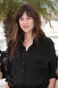 a woman with long hair standing in front of a palm tree wearing a black shirt