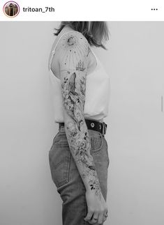 a woman with a tattoo on her arm and leg, leaning against a wall wearing jeans