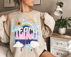 "Our retro teacher sweatshirt is perfect for the holidays and beyond. This super soft crewneck sweatshirt features a retro TEACH with sunflowers, sun, clouds, and rainbows. A fun gift for teachers, principals and parents who always try their best to make your children smile. Retro Teacher Sweatshirt Teach Trendy New Teacher Gifts ideas Elementary Middle School Kindergarten crewneck principal learning preschool **Don't see a size or COLOR that you want? Just ask >> A premium soft blend UNISEX swe Teacher Gifts Ideas, Clouds And Rainbows, Learning Preschool, New Teacher Gifts, Sun Clouds, School Kindergarten, Teacher Sweatshirt, New Teacher, Child Smile