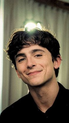 a young man smiling at the camera in front of a window with light shining on him