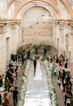 a wedding ceremony in an old building with white flowers and greenery on the aisle