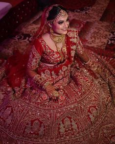 a woman sitting on top of a bed wearing a red and gold wedding dress with an elaborate