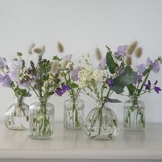 four glass vases with flowers in them sitting on a shelf