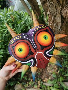 a person holding up a colorful mask in front of a tree