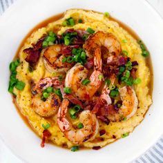 a white bowl filled with mashed potatoes topped with shrimp and green onion garnish