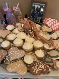 a table topped with lots of cupcakes covered in frosting and decorated like barbie dolls