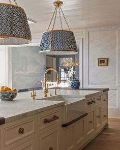 a large kitchen with marble counter tops and gold accents on the island, along with two hanging lights