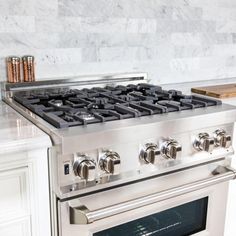 a stainless steel stove top oven in a kitchen with marble counter tops and white cabinets