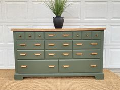 a green dresser with drawers and a plant in the middle on it's top