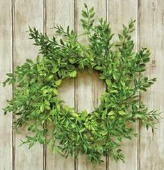 a green wreath hanging on the side of a wooden fence with leaves and branches around it