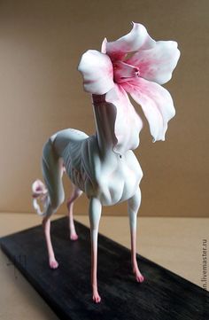 a small white and pink animal standing on top of a wooden table next to a flower