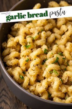 a bowl filled with pasta and parsley on top of a wooden table next to a sign that reads garlic bread pasta