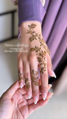 a woman's hands with henna tattoos on them and her hand holding another person's hand