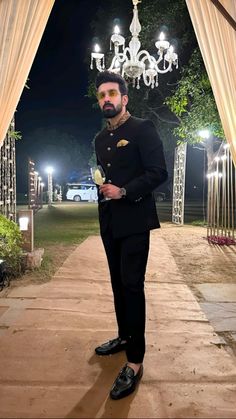 a man in a tuxedo standing under a chandelier