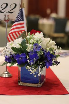 a blue vase filled with flowers on top of a red table cloth next to an american flag