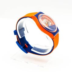 an orange and blue watch sitting on top of a clear stand with a white background