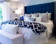 a bedroom with white and blue bedding, pillows and blankets on the headboard