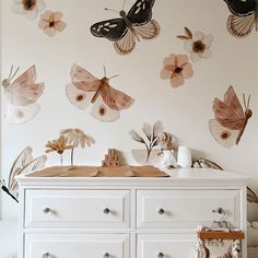 a white dresser topped with lots of drawers next to a wall covered in butterfly decals