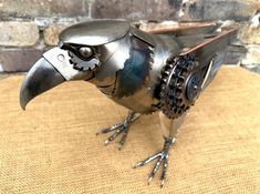 a metal bird sculpture sitting on top of a burlap covered table next to a brick wall