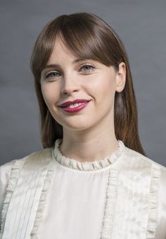 a woman with long hair wearing a white blouse and red lipstick smiling at the camera