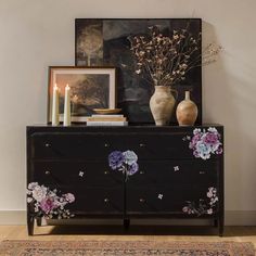 a dresser with flowers painted on it next to a painting and two candles in vases