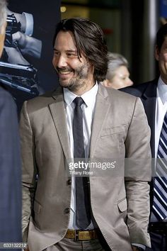 a man in a suit and tie smiles as he walks down the red carpet at an event