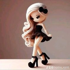 a knitted doll with long blonde hair and black shoes is posed on a table