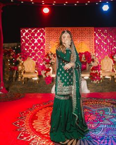 a woman in a green lehenga standing on a colorful carpet with lights behind her