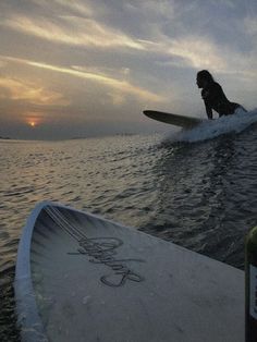 a person riding a surfboard on top of a body of water in the sunset