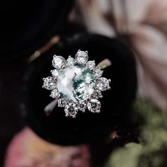 an engagement ring with a large green stone surrounded by small white diamonds on top of it