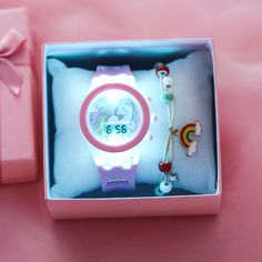 a pink watch in a gift box next to a bracelet and keychain with a unicorn on it