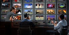 two people sitting at a desk in front of monitors with images on the wall behind them