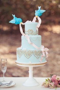 a wedding cake with blue frosting and two birds on top is sitting on a table