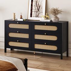 a black dresser with wicker drawers and gold handles in a white room next to a bed