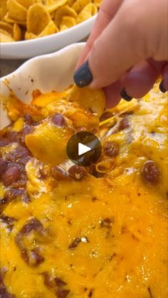 a person is dipping some food into a casserole dish with tortilla chips