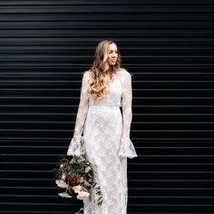 a woman standing in front of a black wall wearing a long sleeved wedding dress