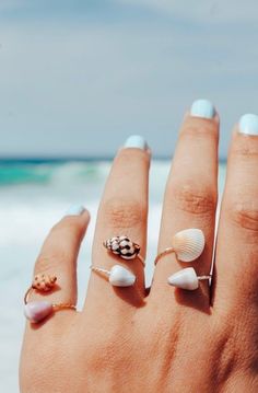 a woman's hand with seashells and rings on it