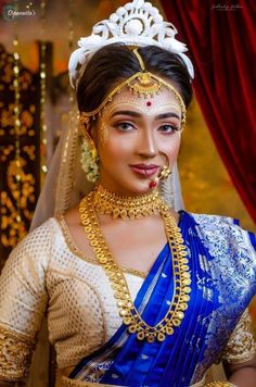 a woman wearing a blue and gold bridal outfit with jewelry on her head, in front of a red curtain