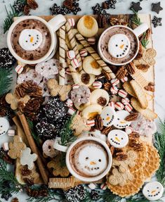 two cups of hot chocolate surrounded by cookies, marshmallows and pretzels