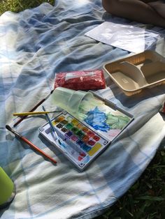 an artist's palette and watercolors on a blanket in the grass next to other items